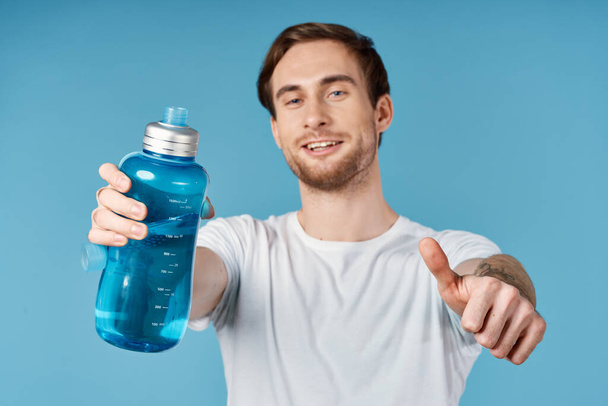 άνθρωπος σε λευκό t-shirt μπουκάλι νερό σβήσιμο δίψα περικοπή προβολή μπλε φόντο - Φωτογραφία, εικόνα