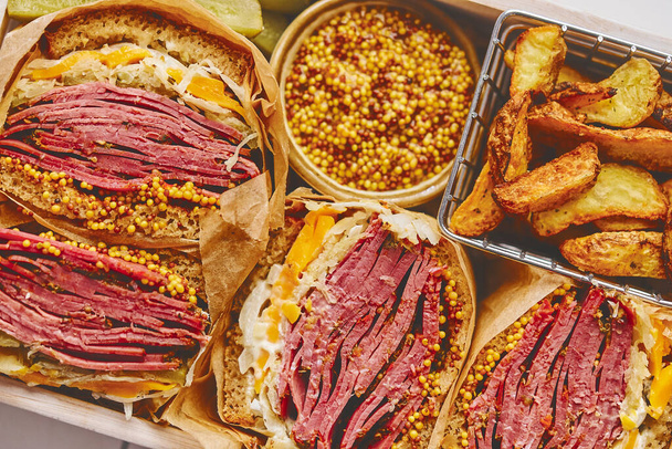 Enormous sandwiches with pastrami beef in wooden box. Served with baked potatoes, pickles - Foto, imagen
