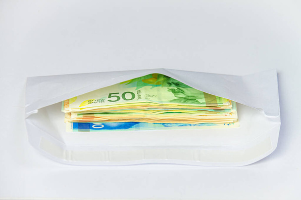 A bundle of new Israeli shekels bills lie in a mail envelope on a light background. - Photo, Image