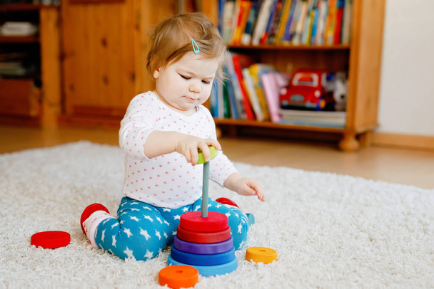 Entzückend süße schöne kleine Mädchen spielen mit pädagogischen Holzspielzeug zu Hause oder im Kinderzimmer. Kleinkind mit bunter Stapelpyramide und Musikspielzeug. Glückliches gesundes Kind, das Spaß an verschiedenen Spielzeugen hat - Foto, Bild