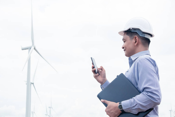 Ingegnere di successo mulini a vento utilizzando smartphone e tenendo il computer portatile con la turbina eolica in background - Foto, immagini