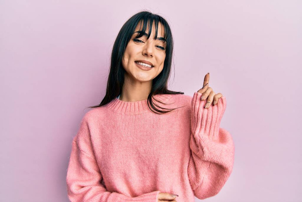 Young brunette woman with bangs wearing casual winter sweater with a big smile on face, pointing with hand and finger to the side looking at the camera.  - Φωτογραφία, εικόνα
