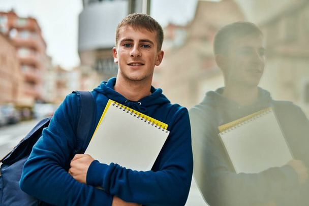 Fiatal szőke diák mosolyog boldog gazdaság notebook az egyetemen. - Fotó, kép