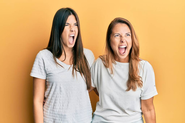 Spaanse familie van moeder en dochter in casual wit tshirt boos en gek schreeuwend gefrustreerd en woedend, schreeuwend van woede. woede en agressief concept.  - Foto, afbeelding
