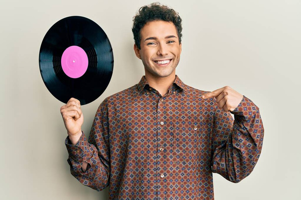 Mladý pohledný muž s vinylovým diskem ukazující prstem na jednoho samolibého šťastného a hrdého  - Fotografie, Obrázek