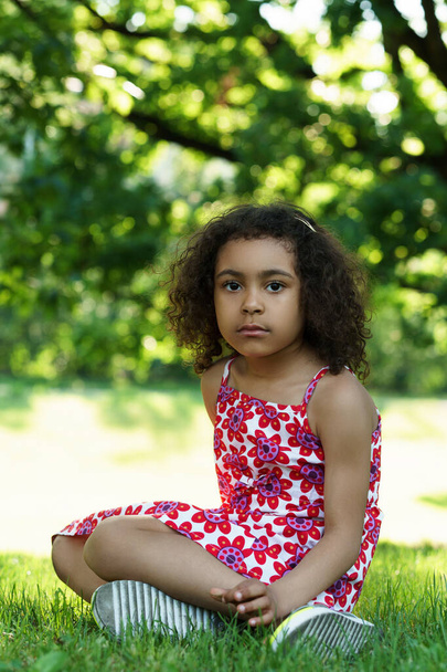 Cute little African girl sitting on a grass in a city park - Fotoğraf, Görsel