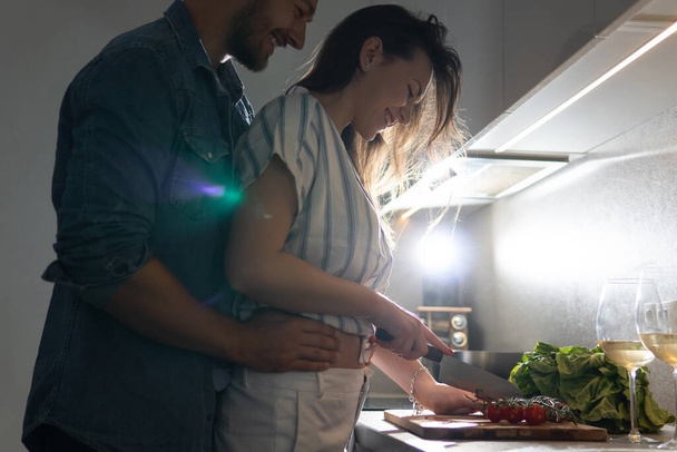 Young couple cooking tasty dinner together in a kitchen at evening - Photo, Image