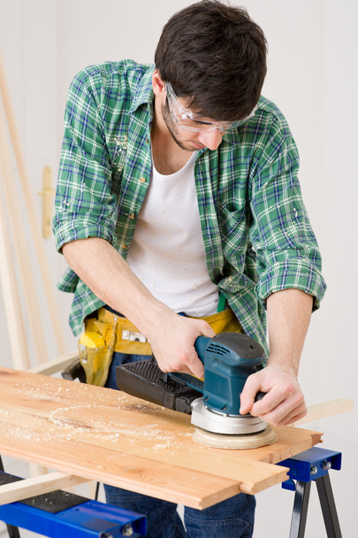 Home improvement - handyman sanding wooden floor in workshop - Foto, Bild