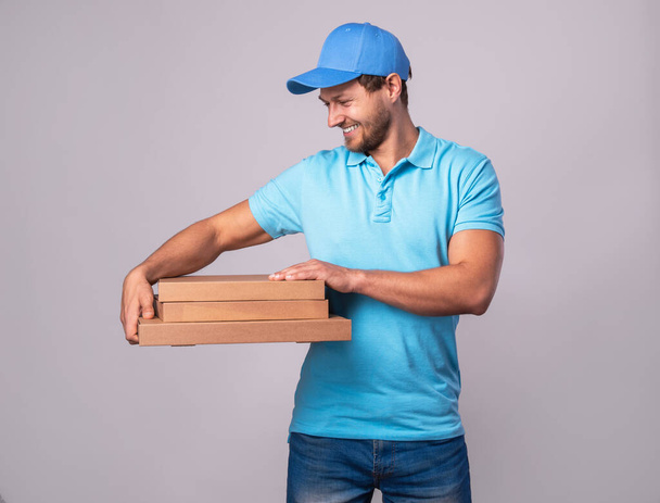 Young delivery man is holding boxes with a delicious pizza  isolated on gray backgroun - Foto, Bild