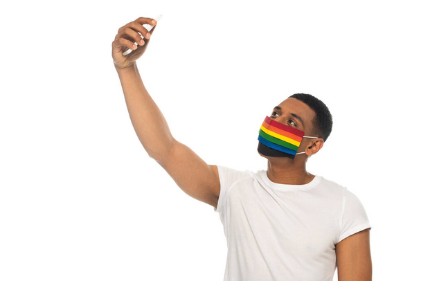 Αφροαμερικάνος άνδρας που φοράει ιατρική μάσκα Igbt χρωμάτων και βγάζει selfie απομονωμένη σε λευκό - Φωτογραφία, εικόνα