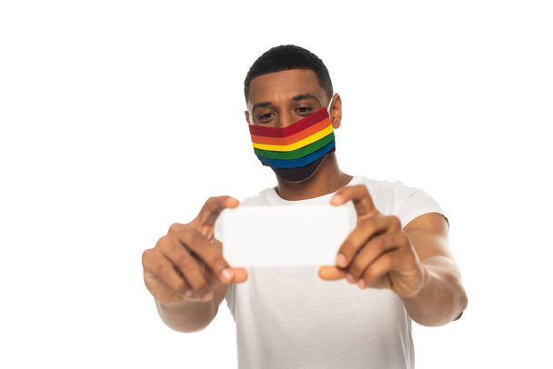 africký Američan muž nosí bezpečnostní masku v lgbt barvách a přičemž selfie na smartphone izolované na bílém - Fotografie, Obrázek