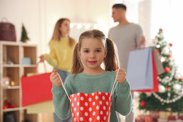 Little girl with bag near her parents in store. Family Christmas shopping - Foto, Imagen