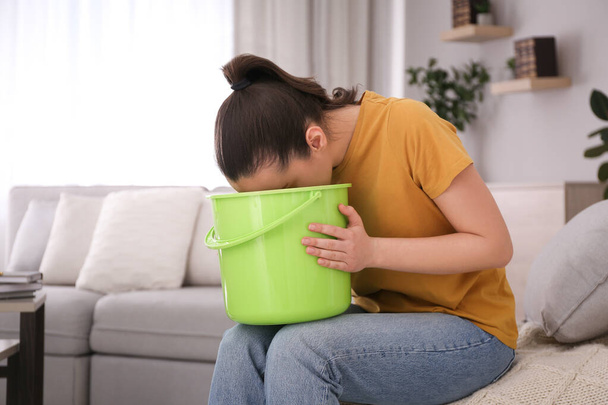 Young woman with bucket suffering from nausea at home. Food poisoning - Foto, immagini