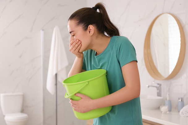 Young woman with bucket suffering from nausea in bathroom. Food poisoning - Foto, immagini