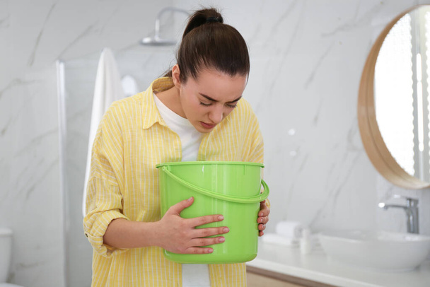 Young woman with bucket suffering from nausea in bathroom. Food poisoning - Foto, immagini