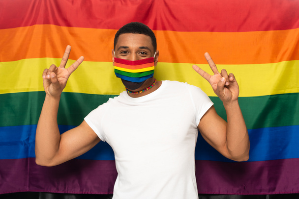 african american man in rainbow colors medical mask showing peace sign on background of lgbt flag - Foto, immagini