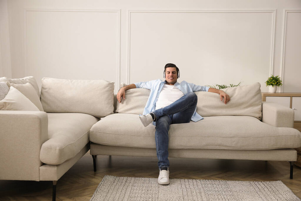 Man with headphones sitting on comfortable sofa in living room - Zdjęcie, obraz
