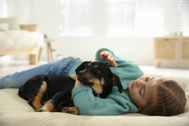 Klein meisje met schattige puppy liggend op zacht kussen thuis - Foto, afbeelding