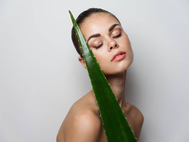 young woman with closed eyes naked shoulders and aloe leaf - Fotoğraf, Görsel