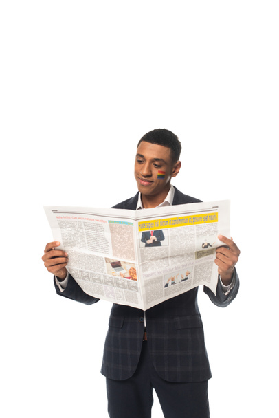 θετική αφροαμερικανός επιχειρηματίας με σημαία Igbt ζωγραφισμένα στο πρόσωπο ανάγνωση εφημερίδα απομονώνονται σε λευκό - Φωτογραφία, εικόνα