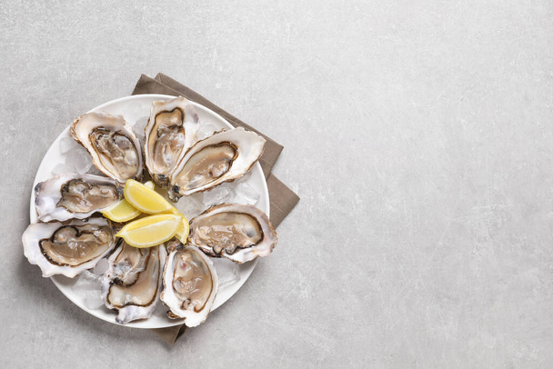 Delicious fresh oysters with lemon slices on light grey table, top view. Space for text - Φωτογραφία, εικόνα
