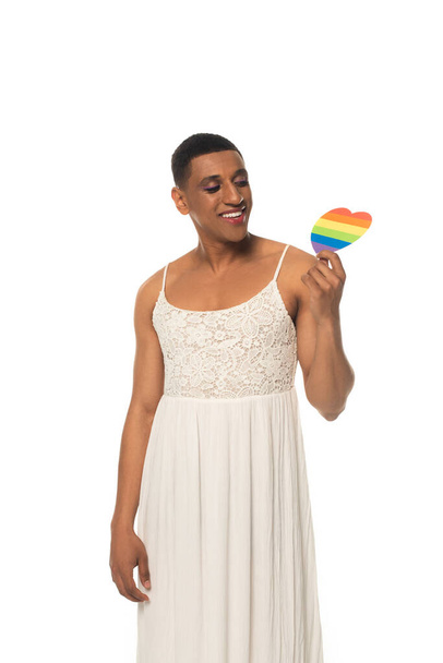 vreugdevolle Afrikaanse Amerikaanse transgender man in jurk met lgbt kleuren papier hart geïsoleerd op wit - Foto, afbeelding