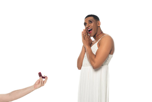 muž drží snubní prsten v blízkosti ohromený africký americký transsexuál izolované na bílém - Fotografie, Obrázek
