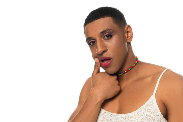 afro-americana transgênero mulher esfregando batom enquanto olha para a câmera isolada no branco - Foto, Imagem