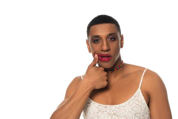 african american transgender man in sundress looking at camera while smearing lipstick isolated on white - Foto, Bild
