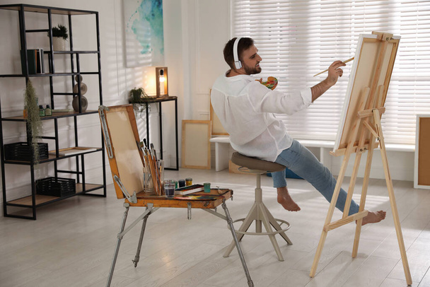 Young man painting on easel with brush in artist studio - Foto, Bild