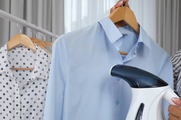 Woman steaming shirt on hanger at home, closeup - Photo, image