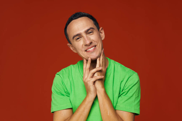 Homme joyeux en t-shirt vert sourire émotions studio fond rouge - Photo, image