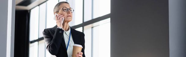 Mature businesswoman with coffee to go talking on smartphone, banner  - Foto, afbeelding