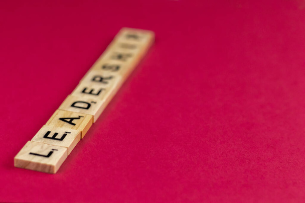 Primer plano de la palabra Liderazgo en bloques de madera con espacio de copia y algunas letras desenfocadas sobre fondo rosa - Foto, Imagen