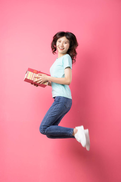 vrouw holding gift box springen met vrolijke expressie op de achtergrond - Foto, afbeelding