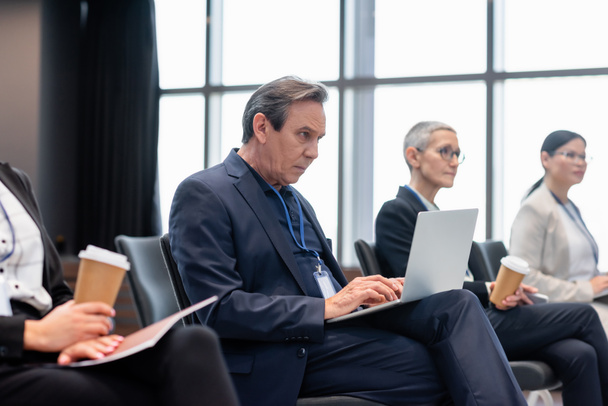 Businessman using laptop near colleagues during seminar    - Photo, Image