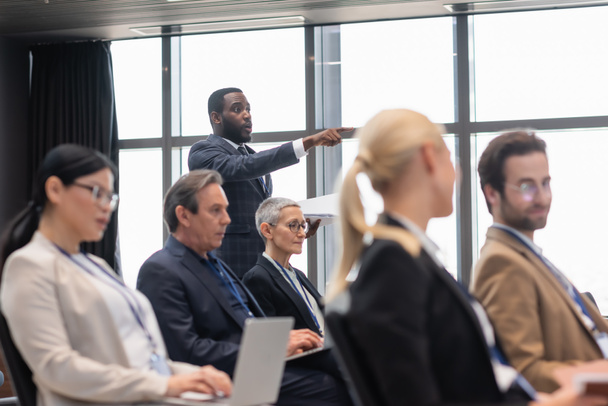 Uomo d'affari afroamericano che punta il dito verso colleghi sfocati in sala conferenze  - Foto, immagini