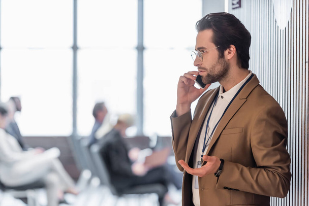 Вид збоку молодого бізнесмена, що розмовляє по мобільному телефону біля конференц-залу
  - Фото, зображення