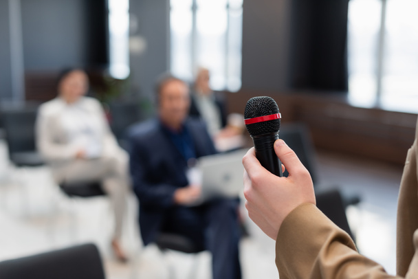 speaker holding microphone near blurred participants during business conference - Photo, Image