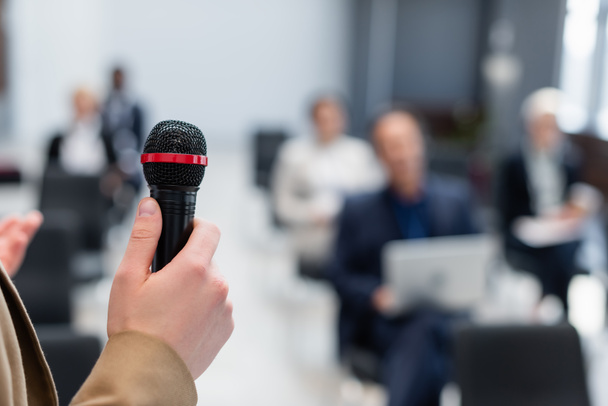 Redner hält Mikrofon in der Nähe verschwommener Geschäftsleute während des Seminars - Foto, Bild