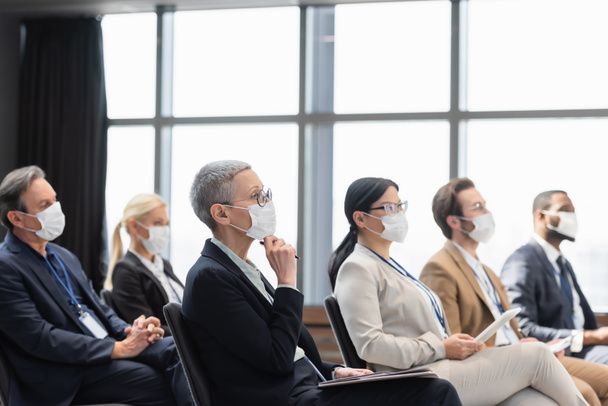 Multiethnische Geschäftsleute in medizinischen Masken sitzen während der Konferenz im Konferenzraum - Foto, Bild