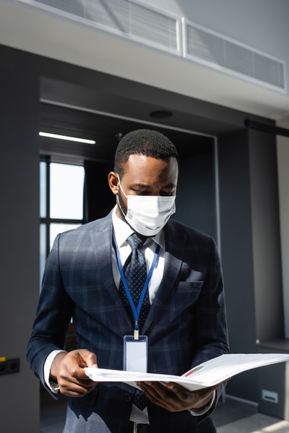 africano americano hombre de negocios en médico máscara celebración carpeta con documentos en la oficina - Foto, Imagen