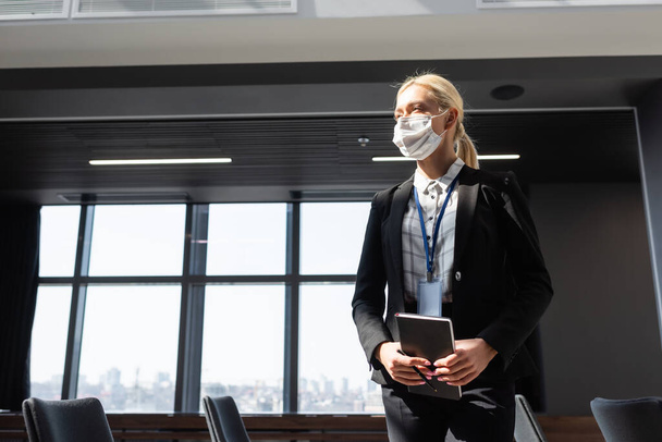 blonde businesswoman in medical mask standing with notebook in conference room - Foto, immagini