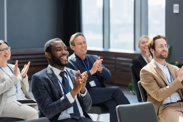Afrikaans-Amerikaanse zakenman applaudisseren met multi-etnische deelnemers tijdens seminar - Foto, afbeelding