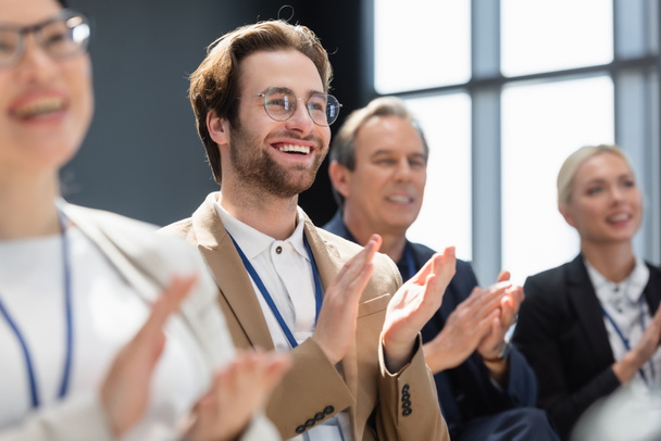 selective focus of young businessman applauding with multiethnic colleagues on seminar - Photo, Image