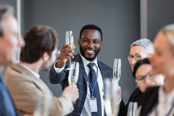 selective focus of african american businessman holding champagne glass near interracial colleagues - Fotografie, Obrázek