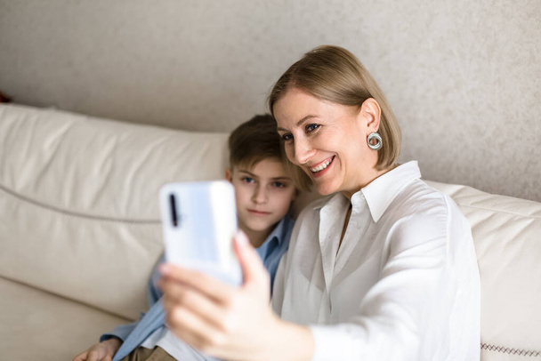 Boy and adult woman take a selfie on the phone while sitting on the couch. - Foto, Imagem