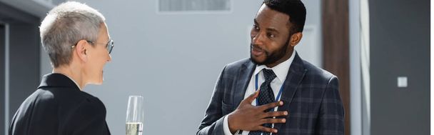 afrikkalainen amerikkalainen liikemies kädestä rinnassa puhuessaan kollegansa, banneri - Valokuva, kuva