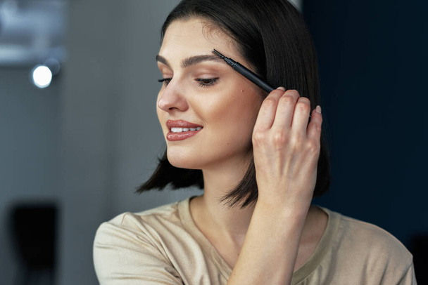 A beautiful young woman combing her eyebrows during doing makeup. - Photo, Image