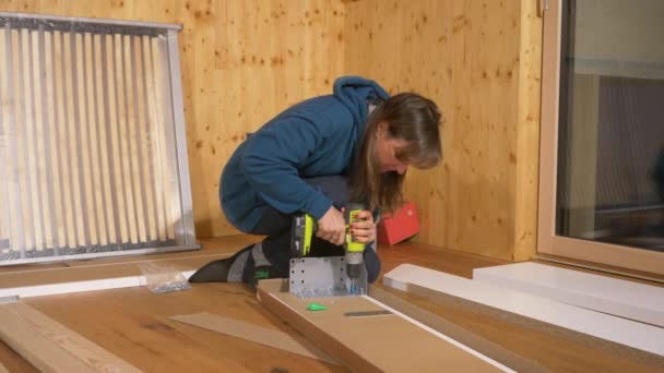 CERRAR: La mujer utiliza un taladro eléctrico para atornillar una pieza de metal en una tabla de madera. - Imágenes, Vídeo